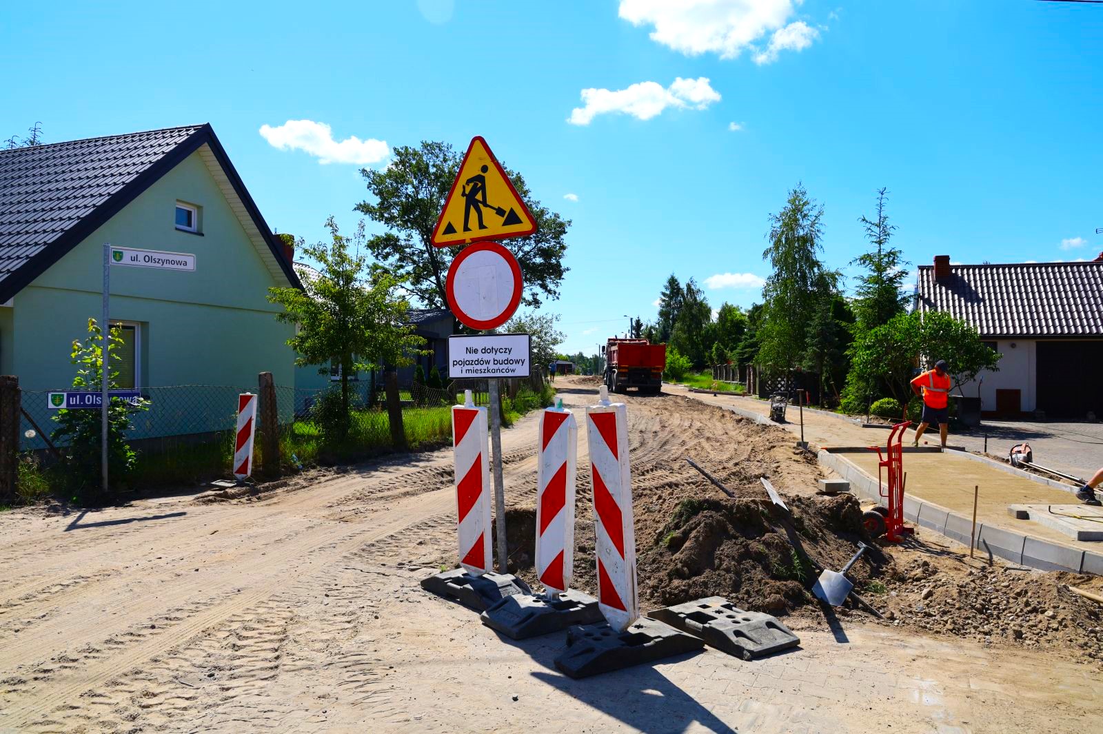 Zdjeci aprzedstawia rozkopana uliće Olszynową, znak zakaz wjazdu i uwaga roboty. w tle samochód ciężarowy i pracownik na chodniku