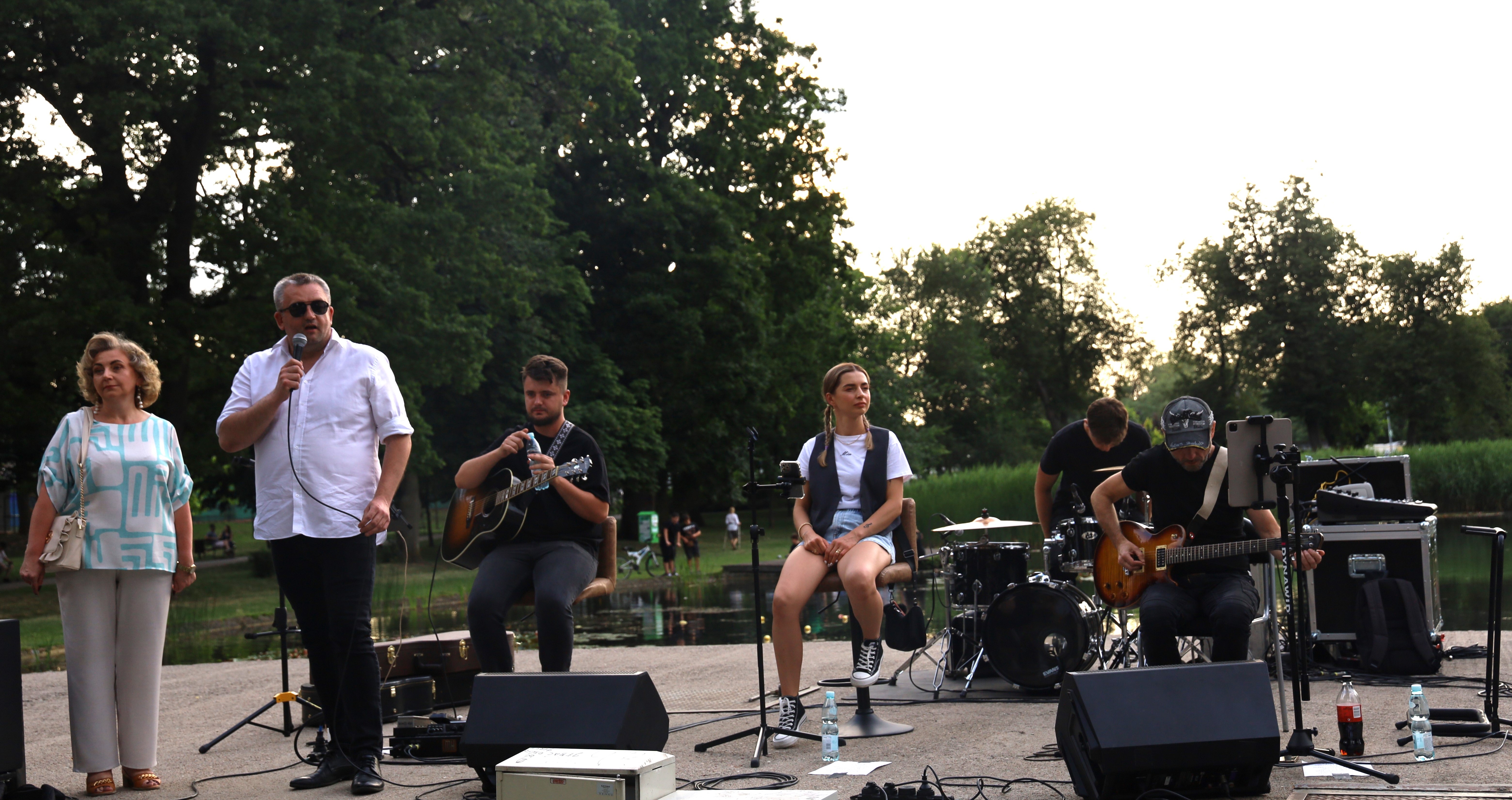 kobieta i mężczyzna przemawiająca do mieszkańców na scenie na której znajduje się zespół