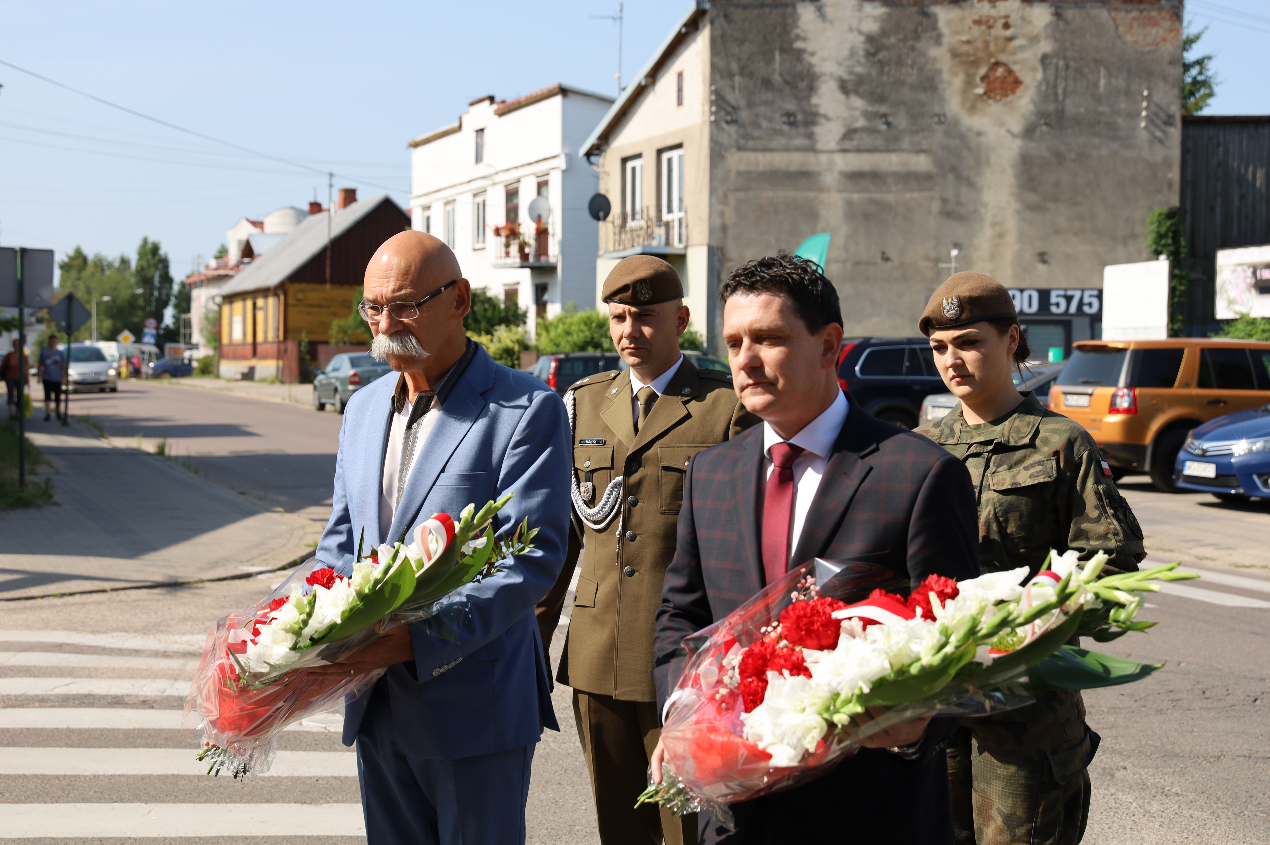 na zdjęciu zastępca burmistrza i starosta powiatu z kwiatami i dwoje żołnierzy z tylu jako delegacja