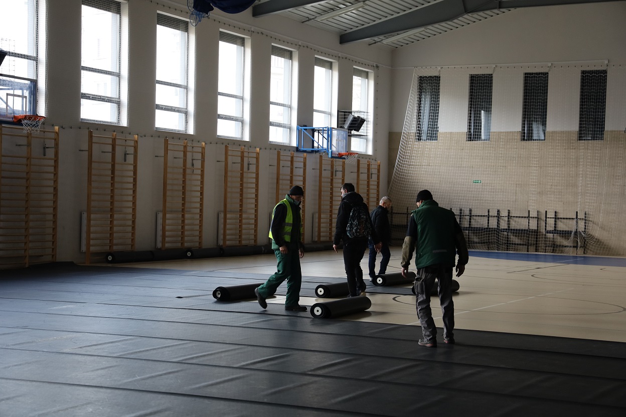 pracownicy ostrowskiej spółdzielni socjalnej zabezpieczają podłogę hali sportowej wykładziną ochronną