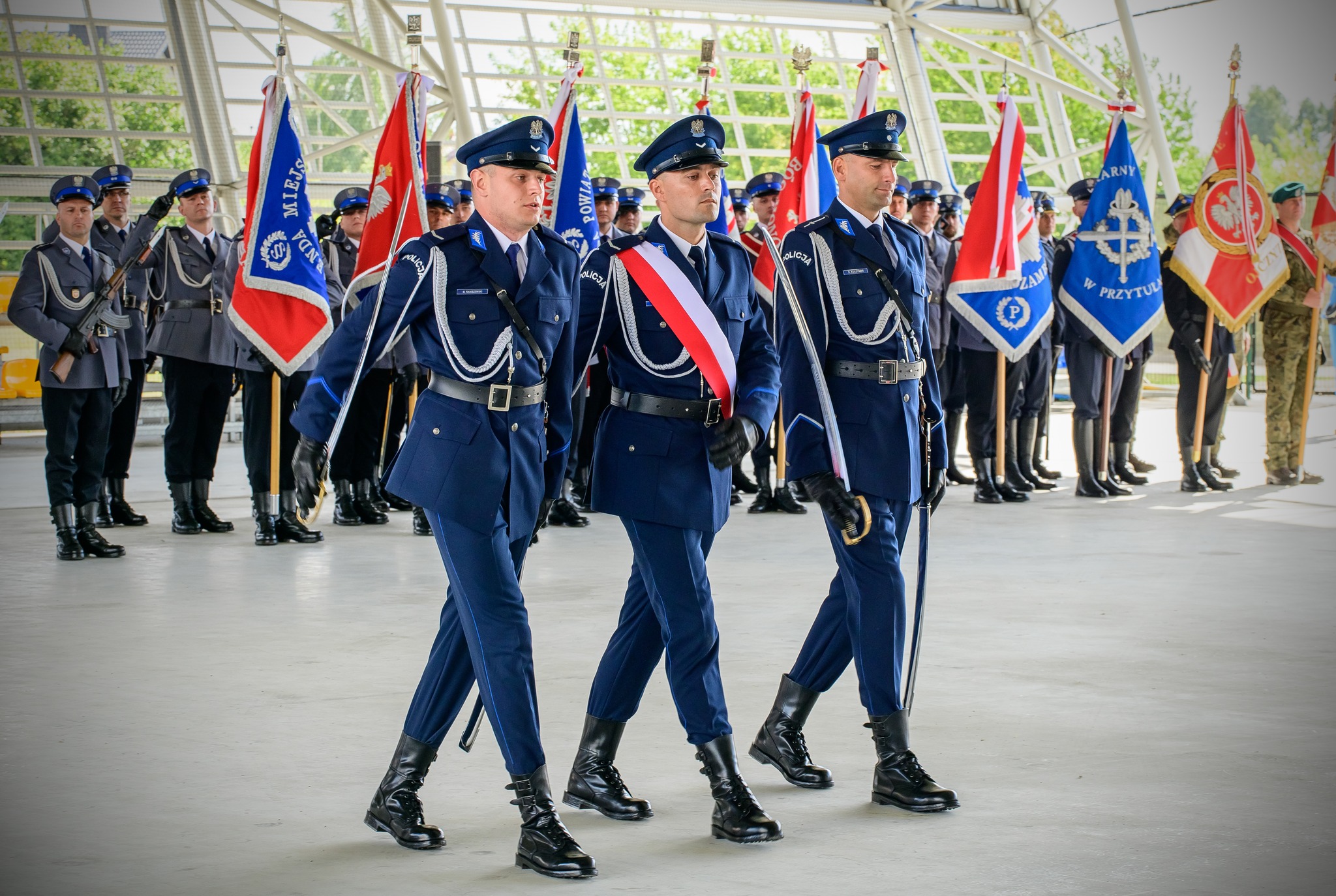 Policjanci niosący sztandar na obiekcie OMEGA, w tle pozostali Policjanci trzymający sztandary