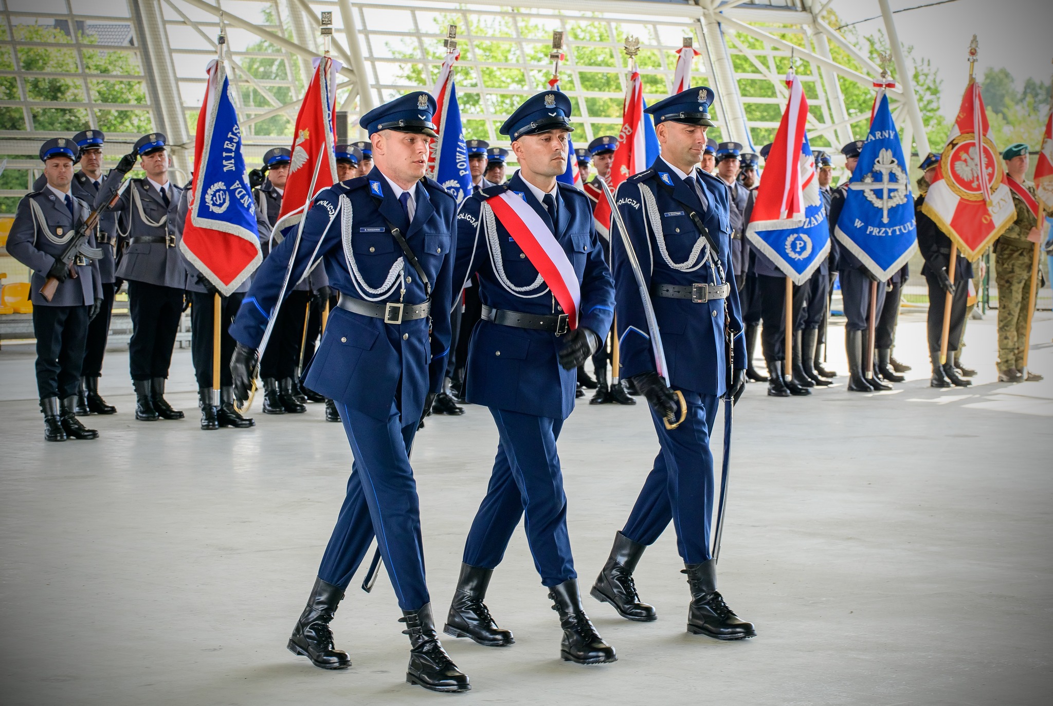 Policjanci niosący sztandar na obiekcie OMEGA, w tle pozostali Policjanci trzymający sztandary 