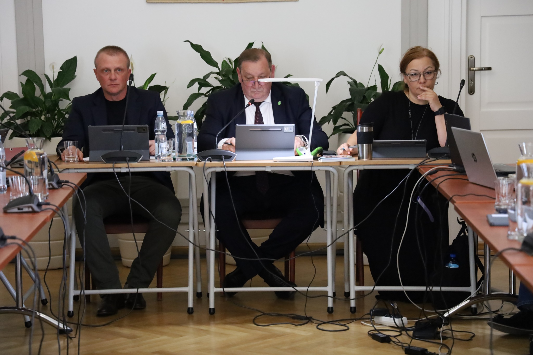 trzy osoby siedzą przy stole patrzą w tablety