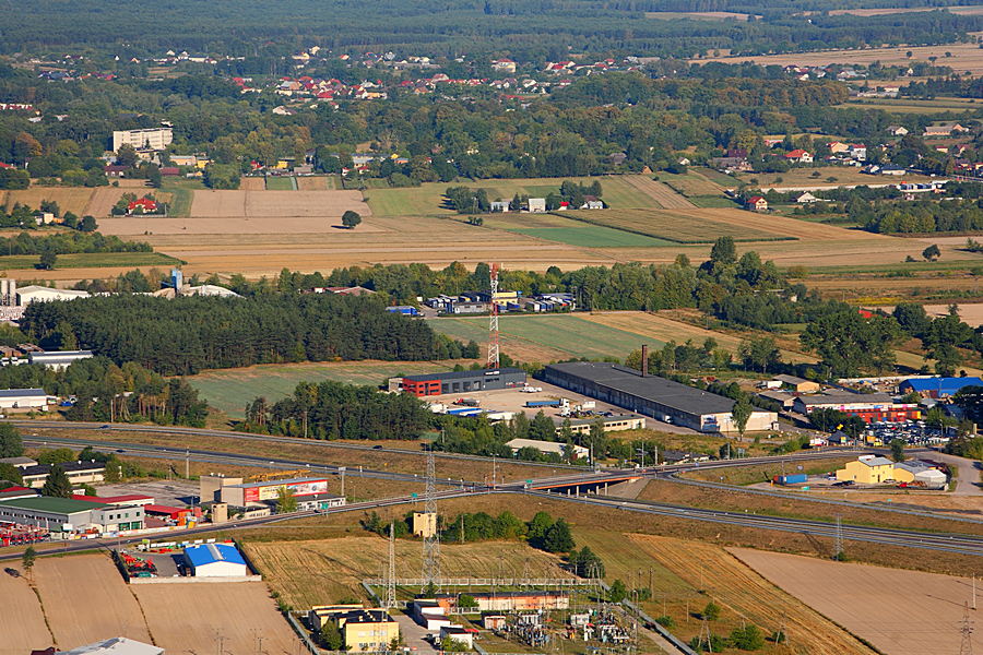 Miasto Ostrów mazowiecka z lotu ptaka, widać pola, działki, fabrykę i domy.