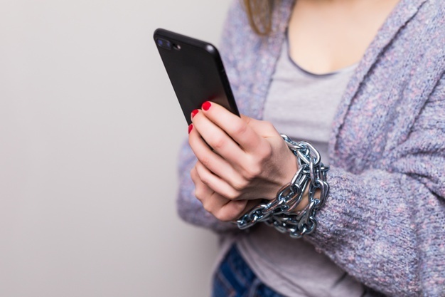 zdjęcie przedstawia kobietę trzymającą telefon, na nadgarstkach ma łańcuchy