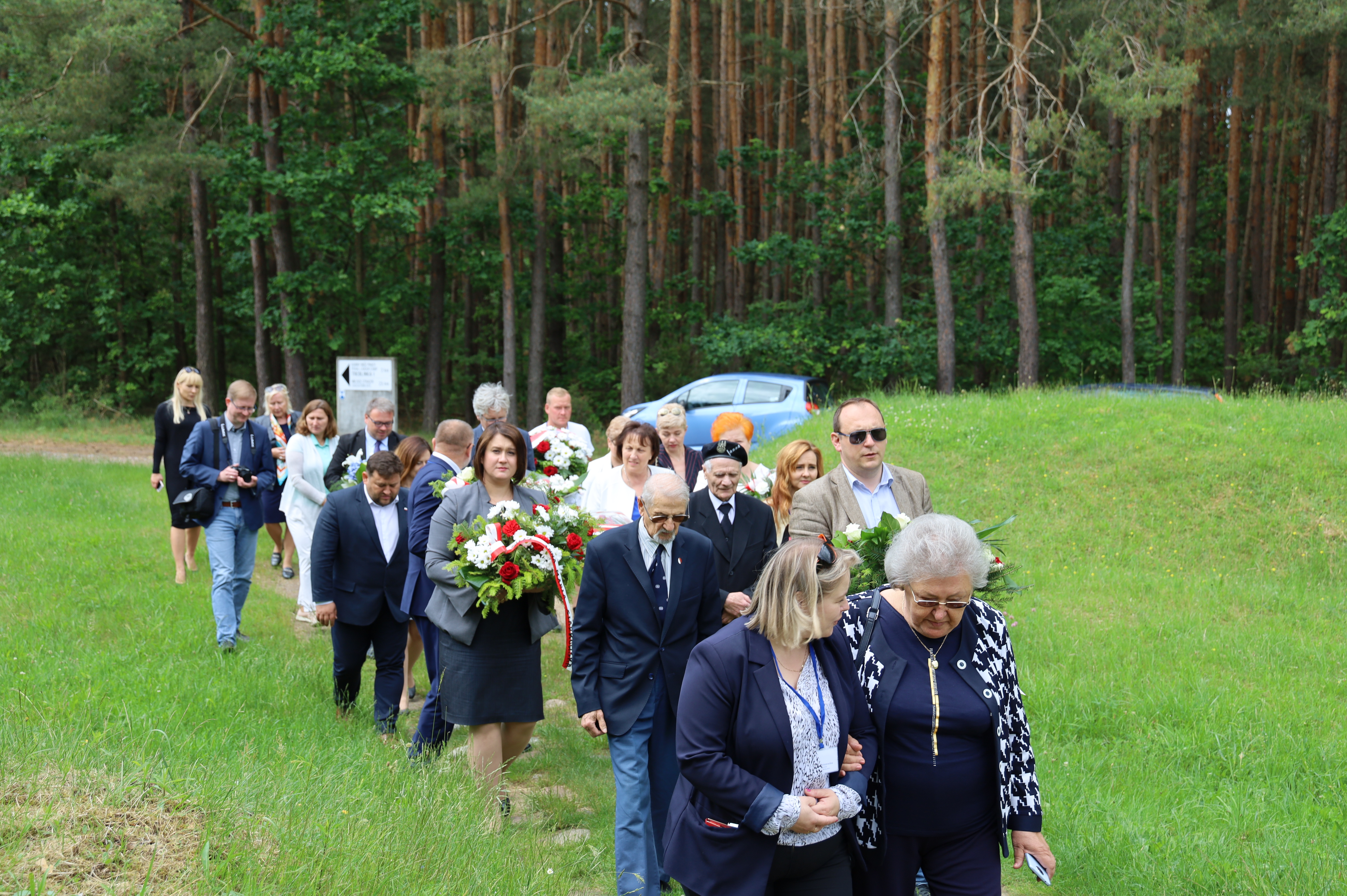 Grupa ludzi idąca z kwiatami przez teren Muzeum Treblinka na obchody uroczystości 
