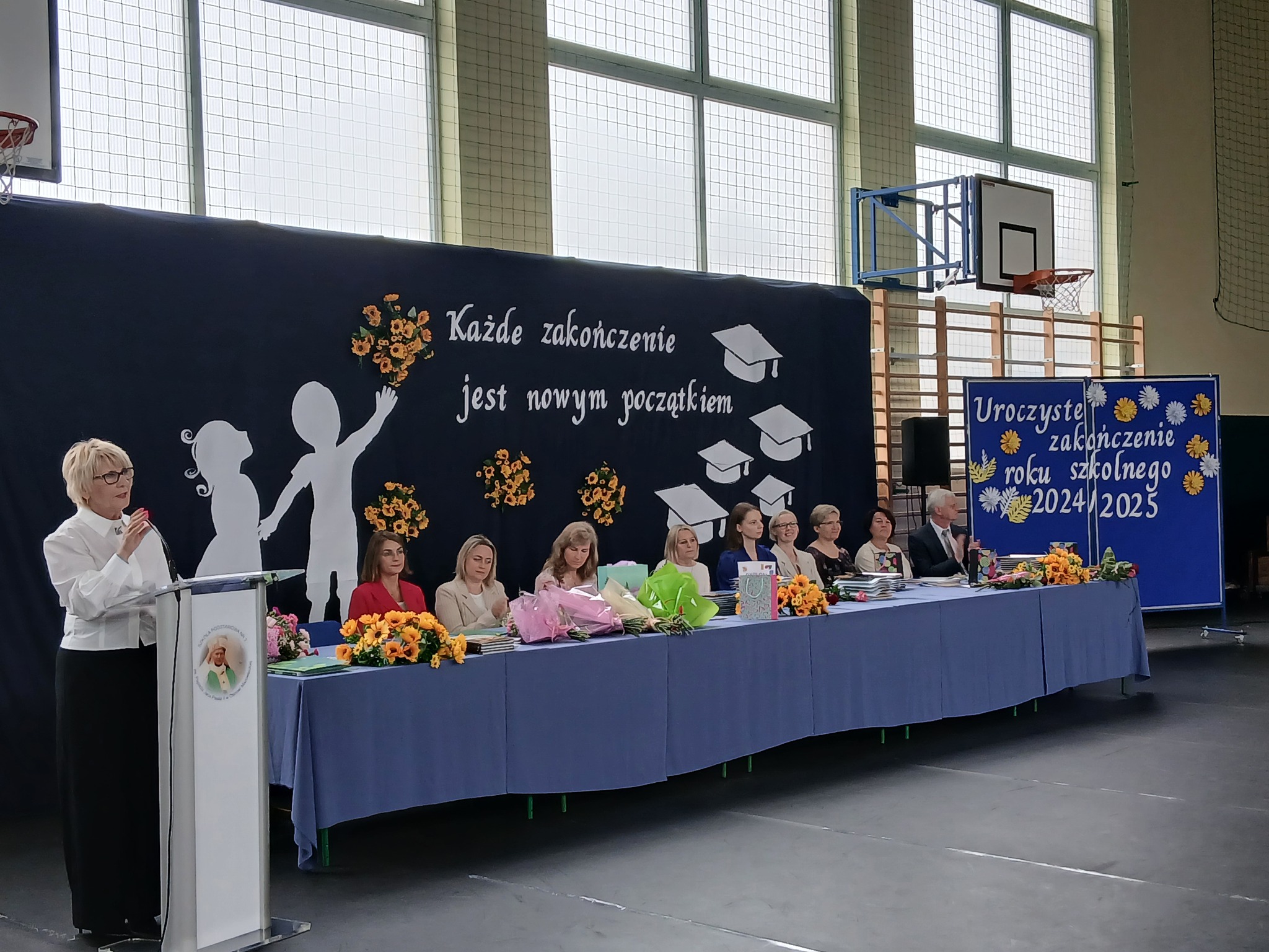 grupa osób siedzi przy stole jedna osoba przemawia